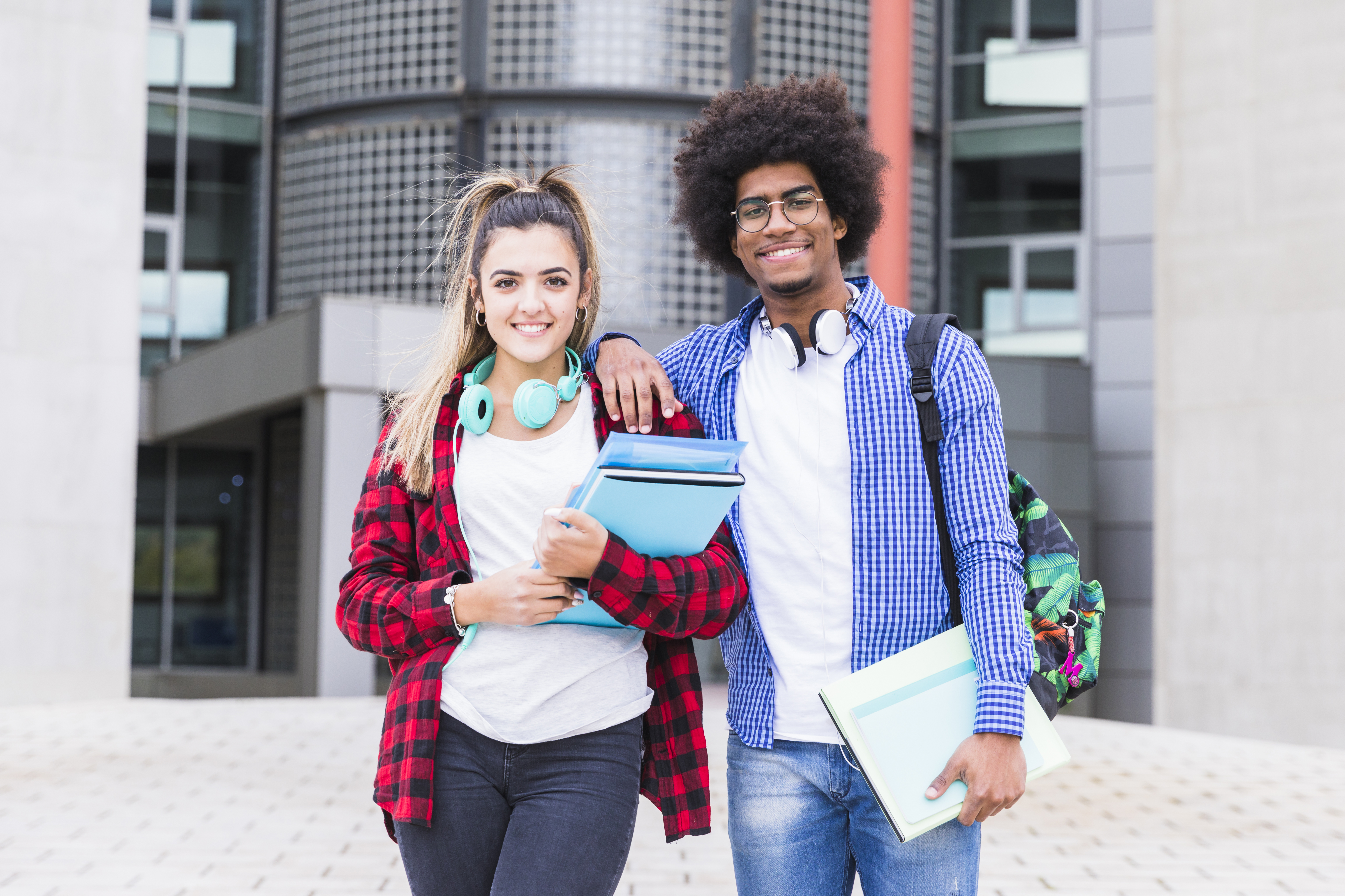 two-happy-young-students-looking-to-camera-standing-in-front-of-university-building